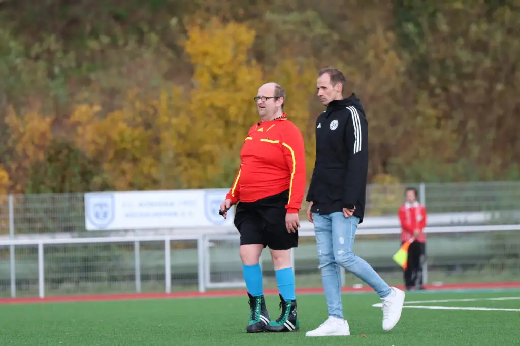 Schiedsrichter und ein Spieler in rotem Trikot auf dem Fußballplatz