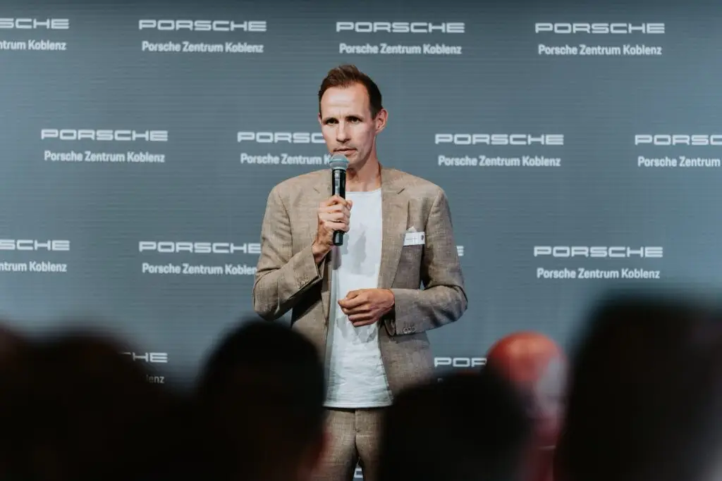 Sascha Stegemann hält einen Vortrag vor einer Wand mit Porsche-Logos