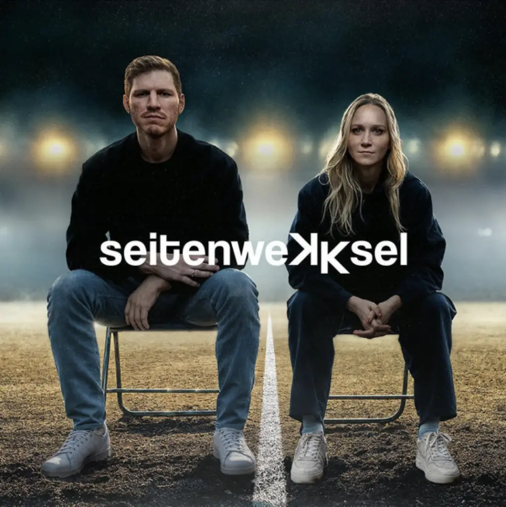 Ein Mann und eine Frau sitzen auf Stühlen auf dem Fußballrasen. Text im Bild: seitenwekksel