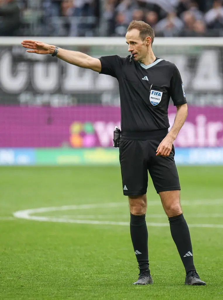 Schiedsrichter Sascha Stegemann pfeift eine Szene auf dem Spielfeld und zeigt nach links